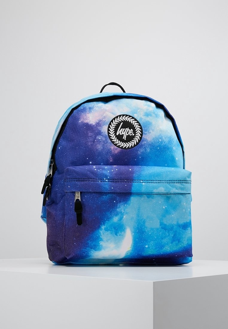 Reppu, jossa on galaksikuvio sinisissä ja purppura sävyissä, mustalla logo-ompeluksella ja vetskarella varustettu etutasku. Valmistettu kestävästä kankaasta.