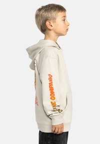 Ljusbeige hoodie med en känguruficka, prydd med färgglada tryckta grafiker på ärmarna och baksidan, tillverkad av mjukt textilmaterial.