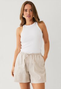 Witte geribde tanktop, lichtbeige shorts met trekkoord. De shorts hebben zijzakken en zijn gemaakt van een zachte, lichte stof met een relaxed fit.