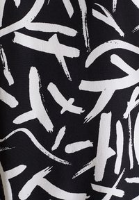 Tissu noir avec des motifs audacieux en coups de pinceau blancs. Le design est abstrait, avec des épaisseurs et des directions de lignes variées.