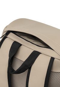 Bézs színű kézitáska sima külsővel, fekete hálós pántokkal és cipzáras tetejével. Díszvarrással ellátott és puha belső bélés jellemzi.