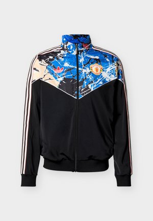 Black Adidas zip-up jacket with blue and white paint splatter design, red Adidas logo, and Manchester United crest on chest.