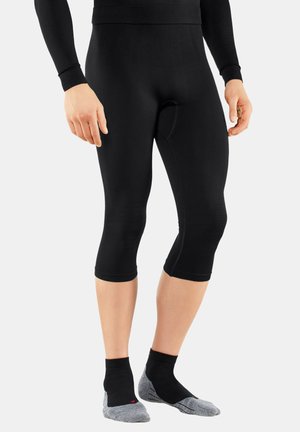 Schwarze Dreiviertellange Leggings mit einer glatten, dehnbaren Textur; kombiniert mit kurzen schwarzen und grauen Socken. Keine sichtbaren Muster.