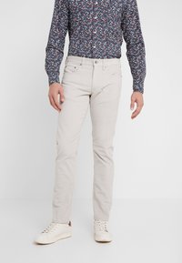 Jasne, dopasowane spodnie wykonane z miękkiego materiału, zestawione z ciemną koszulą w kwiatowy wzór i białymi trampkami.