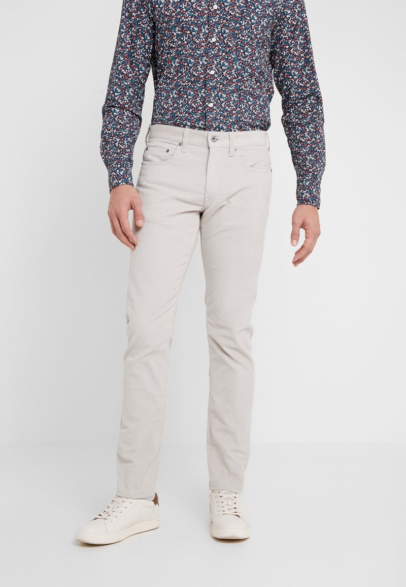 Jasne, dopasowane spodnie wykonane z miękkiego materiału, zestawione z ciemną koszulą w kwiatowy wzór i białymi trampkami.