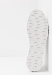 Semelle de basket blanche avec un motif texturé côtelé et des bords arrondis. Marquée "HUGO" et "HUGO BOSS" près du talon.