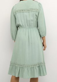 Hellgrünes Midikleid mit Spitzenbesatz am Rückenausschnitt und Saum, geraffter Taille und dreiviertellangen Puffärmeln.