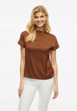 Brun kortärmad blus med rund hals, slät yta, flödande design och lös passform, tillsammans med vita byxor.
