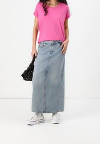 Růžové tričko s krátkým rukávem, modrá maxi sukně z denimu, bílé tenisky. Doplňky zahrnují černou tašku s květinovým vzorem.