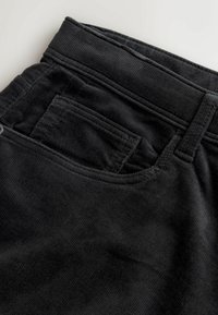 Black corduroy pants featuring a ribbed texture, a rear pocket, and a standard waistband design with stitching accents.