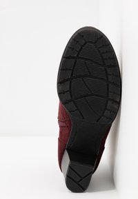 Burgundowe zamszowe botki z teksturowaną czarną gumową podeszwą. Posiadają zamek błyskawiczny z boku oraz słupkowy obcas dla większej stabilności.