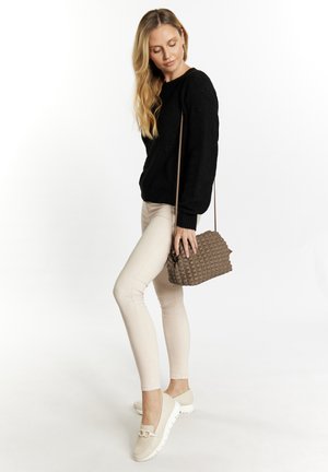 Zwarte gebreide trui, beige aansluitende broek, beige schoenen met een kettingaccent en een bruine textuur schoudertas. Model staat in profiel.