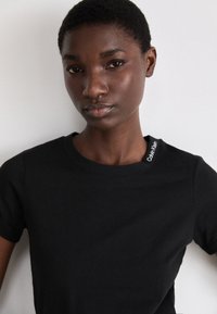 Černé bavlněné tričko s klasickým kulatým výstřihem a krátkými rukávy, které má decentní logo Calvin Klein na švu ramene.