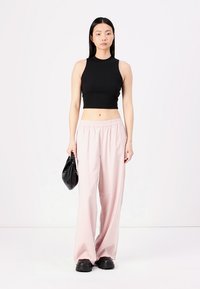 Top corto senza maniche nero, pantaloni larghi rosa chiaro e scarpe nere chunky, abbinati a una borsa nera. Tessuto liscio e vestibilità rilassata.