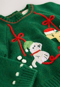 Pull vert tricoté avec accents rouges, présentant des bonhommes de neige brodés et des nœuds. Tissu texturé avec une coupe confortable et un design festif.