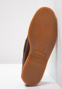 Bruine Timberland schoenzool met niet afgevende rubberen zool, een gestructureerd grip patroon en een in het midden geperst logo tegen een witte achtergrond.