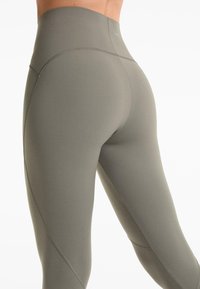 Leggings taille haute en vert olive atténué, fabriqués dans un matériau extensible avec des coutures plates et un design sculptant mettant en valeur la silhouette.