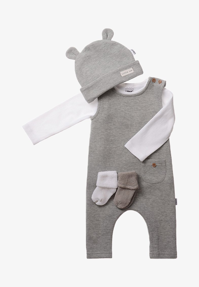 Grau-cotton Overall mit einem weißen Langarmshirt, einer Bärenohrmütze und zwei Paar Stiefelchen. Mit Tasche und Holzknopfdetails.