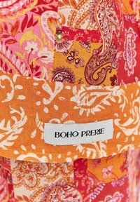 Patchwork látka s živými farbami ako oranžová, ružová a červená, s kvetinovými a paisley vzormi. Nálepka znie "BOHO PRERIE."
