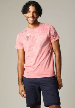 T-shirt graphique rose avec des motifs floraux et de crânes, manches courtes, col rond ; associé à un short bleu marine avec un design texturé.