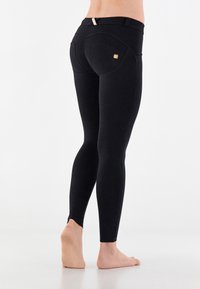 Mustat legginsit, joissa on istuva leikkaus, korkea vyötärö, kaarevat takataskut ja nilkkaleikkaukset. Sileä, joustava kangas.