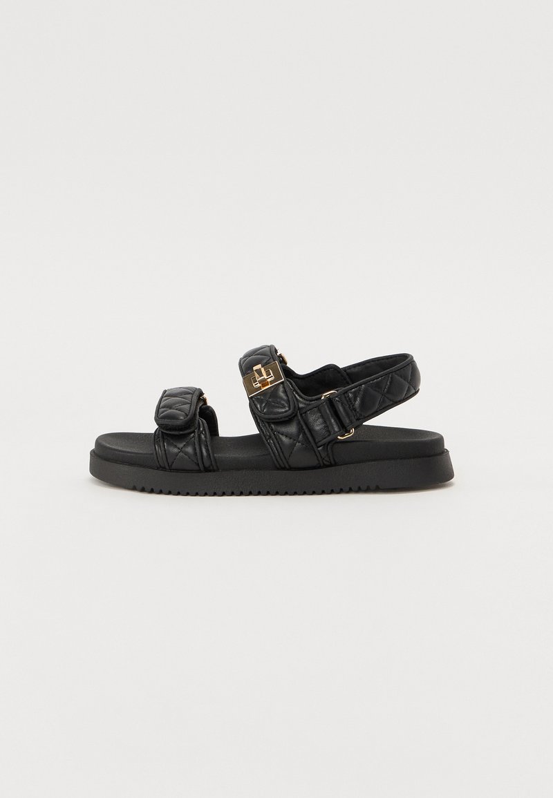 Black quilted sandals with two adjustable straps, gold accents, and a textured black sole. Sleek and contemporary design.
