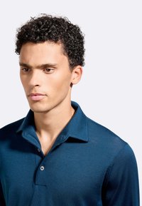 Polo shirt blu navy con colletto a bottoni, texture a coste e maniche corte. Il tessuto appare liscio e leggero.