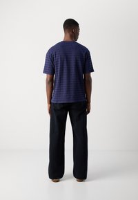 T-shirt bleu marine à manches courtes avec un motif texturé, col rond et coupe décontractée, associé à un pantalon noir à jambe large.