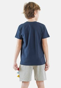 Mørkeblå bomulds t-shirt med korte ærmer, set bagfra; parret med lysegrå shorts med farverige stofdetaljer i siden.