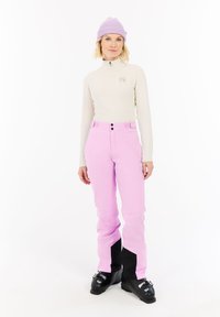 Lichtbeige lange mouw top met een ritssluiting bij de kraag. Felrode broek met een zwart accent op de onderbenen. Zwarte skibotten maken de outfit compleet.