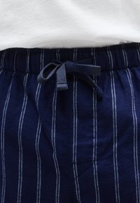 Ναυτικά ριγέ παντελόνια lounge με απαλή υφή, διακοσμημένα με ελαστική μέση και κορδόνι ρολού, συνδυασμένα με ένα λευκό πουκάμισο από πάνω.