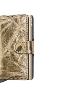 Gold metallic leather wallet with textured surface, snap closure, engraved logo, and silver aluminum cardholder section on the side.