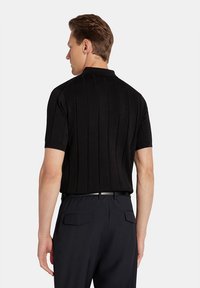 Czarna koszulka polo z krótkim rękawem o pionowej teksturze ribbed, widziana z tyłu. Połączona z ciemnymi spodniami i srebrnym akcentem paska.