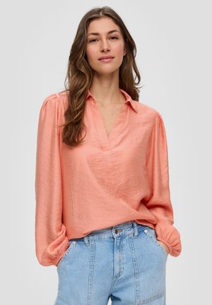 Blouse couleur pêche avec un décolleté en V et des manches longues bouffantes. Fabriquée en tissu léger, elle présente une finition texturée et une coupe décontractée.
