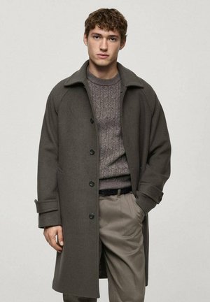 Gray woolen coat with a broad collar, single-breasted design, and black buttons, worn over a textured gray sweater and light trousers.