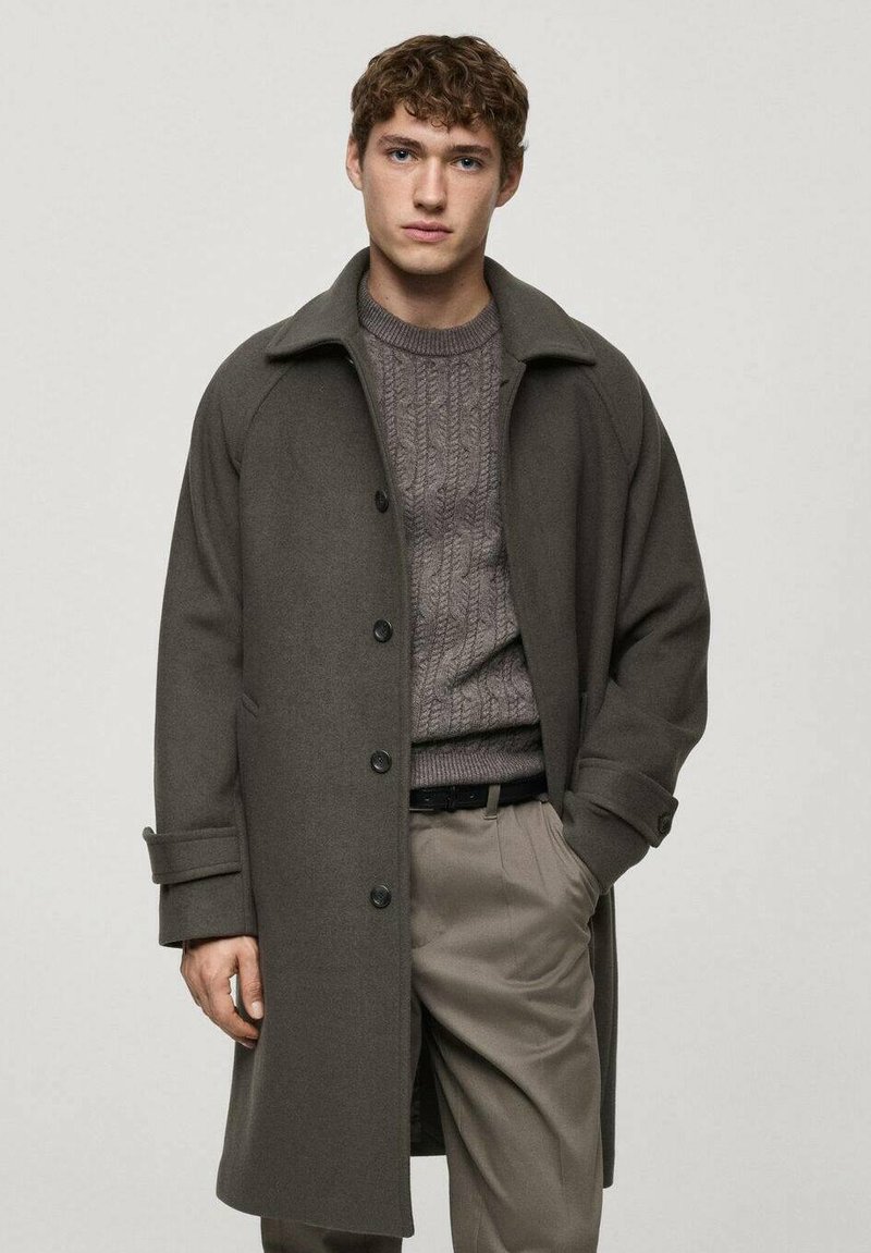 Gray woolen coat with a broad collar, single-breasted design, and black buttons, worn over a textured gray sweater and light trousers.