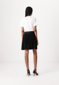 White short-sleeve shirt paired with a black pleated skirt featuring a textured waistband and black high-heeled shoes.