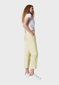 Pantaloni cropped giallo chiaro con tasche laterali, abbinati a una maglietta bianca a maniche corte. Indossati con sneakers bianche con dettagli dorati.