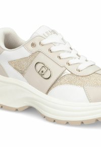 Witte en beige sneaker met stevige zool, witte veters, metallic gaaspanelen en een zilveren logo-embleem aan de zijkant.