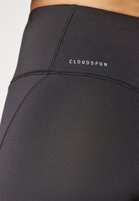 Czarne legginsy wykonane z elastycznej tkaniny o gładkiej strukturze, z wysokim stanem i białym logo "CLOUDSPUN" z tyłu.
