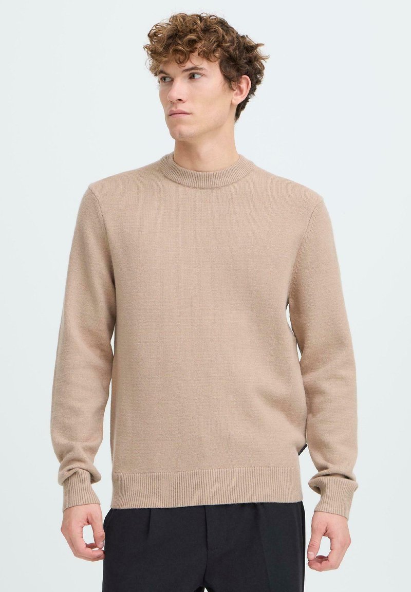 Béžový pletený sveter s okrúhlym výstrihom, dlhými rukávmi, rebrovanými manžetami a lemom. Mäkká textúra a voľný strih. Bez viditeľných vzorov alebo kovania.