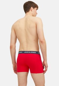 Rote Baumwoll-Boxerbriefs mit einem marineblauen elastischen Bund, der das Logo "JACK & JONES" trägt. Glatte Textur, enganliegendes Design, mittellange Schenkel.