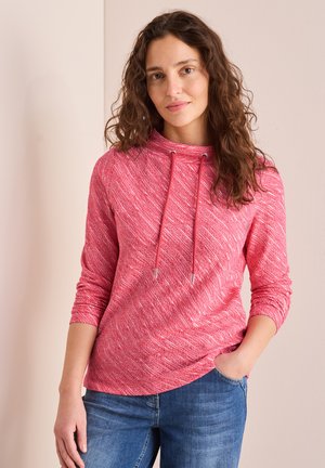 Hoodie rouge texturé avec un col drapé et des détails de cordon. Manches longues et coupe décontractée, associé à un jean bleu.