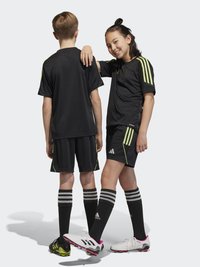 Jersey atlético negro y pantalones cortos con rayas verde neón, combinados con calcetas negras hasta la rodilla y botas de fútbol en negro y blanco con acentos en rosa.