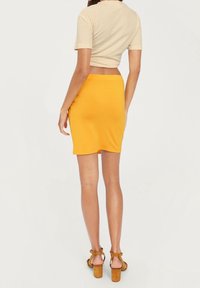 Gonna bodycon gialla con una texture liscia e orlo curvo. Abbinata a una maglietta crop beige e sandali con tacco marroni.