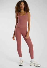 Set van een dusty rose tanktop en legging, gemaakt van rekbare, gladde stof. De top heeft een vierkante halslijn; de leggings zijn aansluitend en hebben een lengte tot de enkel.