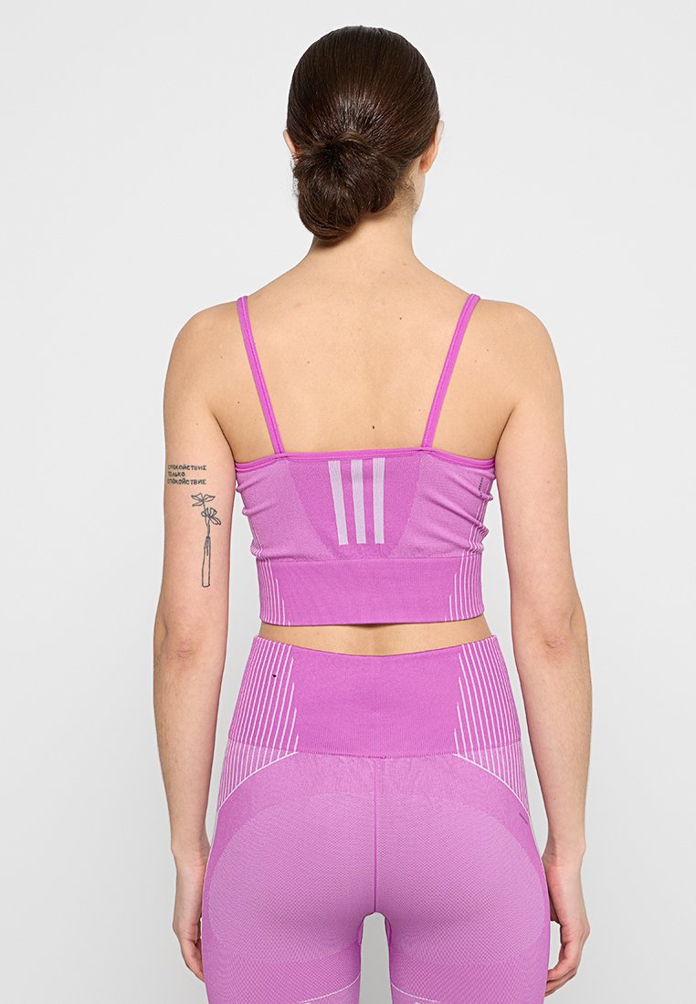 Helles rosa Sport-Crop-Top mit dünnen Trägern, ausgestattet mit drei vertikalen Streifen auf dem Rücken und strukturiertem Gewebe für Atmungsaktivität.