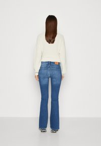 Blå trompetbukser med høj talje, fem lommers design og et brunt lædermærke på bagsiden. Sammen med en cremefarvet strikket sweater.