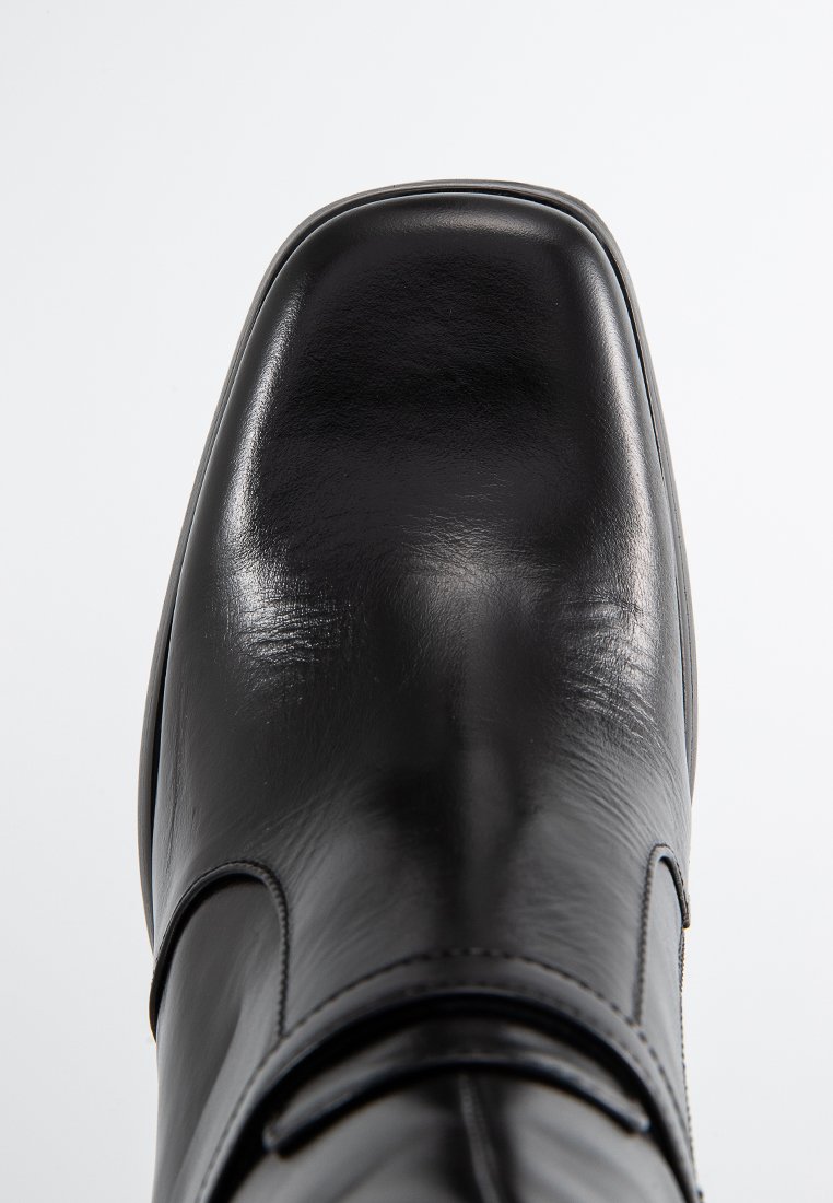 Botte en cuir noir avec un bout carré, texture lisse, couture minimale et un détail de bande latérale. Design épuré et finition soignée.