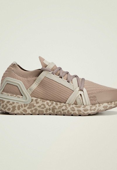 Athletic shoe with a knit upper in light pink, featuring pale accents and a leopard print midsole. The design includes crisscross straps and a unique heel.